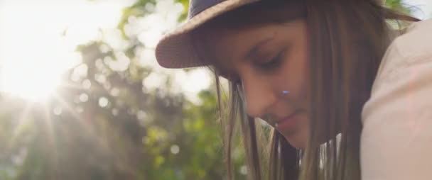 Close up of a beautiful young woman with hat and long brown hair looking down while working in the garden at sunset. Bokeh background and sun flares. SLOW MOTION, SHALLOW DOF, BMPCC 4K.   - Footage, Video