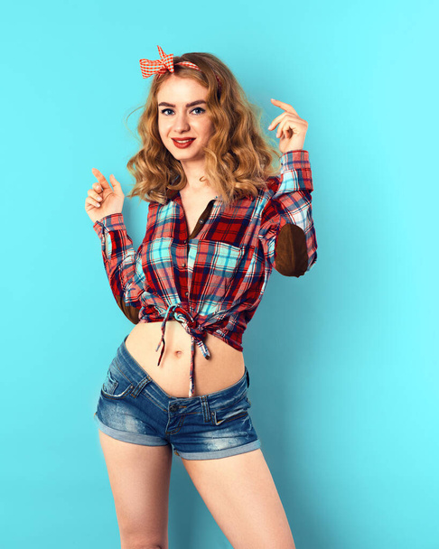 Pin-up girl with curly blond hair with red checkered bow and shirt wearing jeans shorts. - Photo, Image