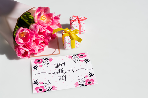 ramo de tulipanes cerca de pequeñas cajas de regalo y tarjeta de felicitación con feliz día de las madres letras en blanco
 - Foto, Imagen