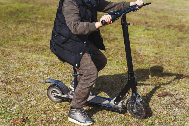 Uma menina monta Kick Scooter com assento na grama no parque. Criança numa scooter. Criança em uma scooter no início da primavera
 - Foto, Imagem