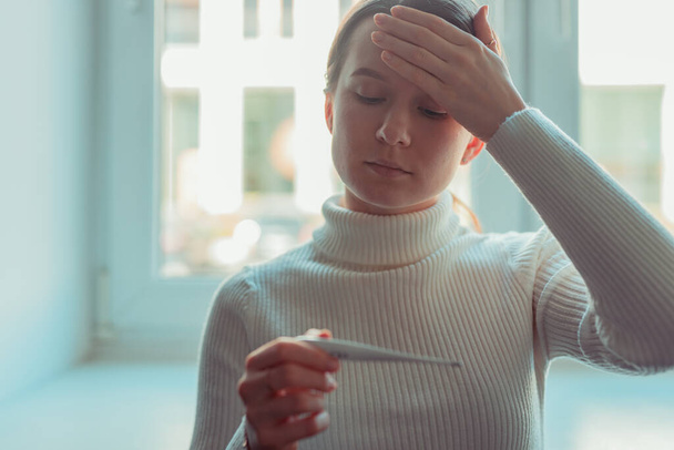 European woman checking high temperature with thermometer. Corona virus infection symptoms headache and in more severe cases, pneumonia - Valokuva, kuva