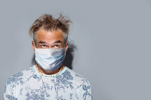 Funny mature man with messy hair wearing protective mask over light background - Foto, Bild
