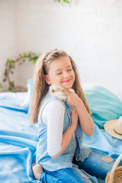 Cute teenage girl in jeans with an Easter rabbit in a bright spring room decorated for Easter. Happy easter - Foto, Imagen