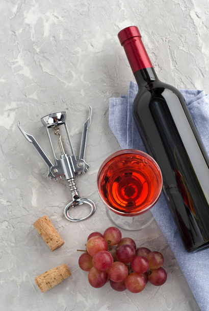 Láhev vína, sklenice vína, svazek růžových hroznů a vývrtka na šedém texturovaném pozadí. Horní pohled. - Fotografie, Obrázek
