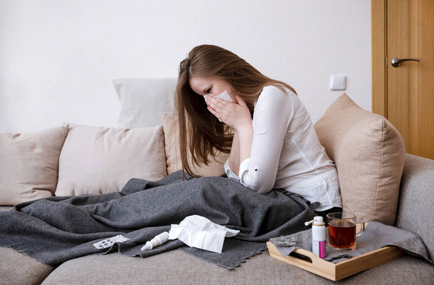 1 белая женщина в белой рубашке сидит на диване и чихает, болезнь, больной, носовой платок, лекарства, одеяло
 - Фото, изображение