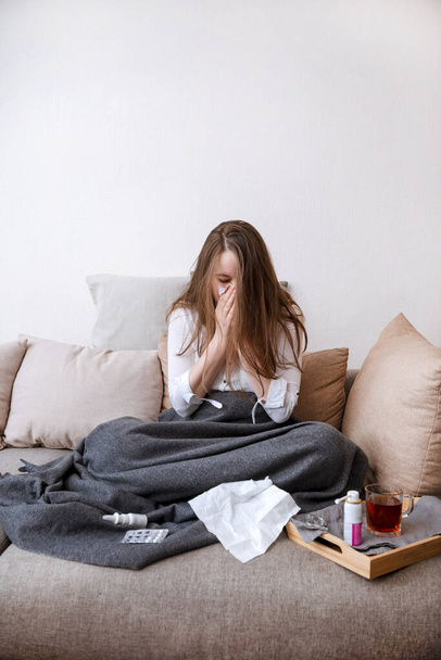 1 white woman in a white shirt sitting on the couch and sneezing, illness,  sick,  medication, blanket, handkerchief, - Foto, imagen