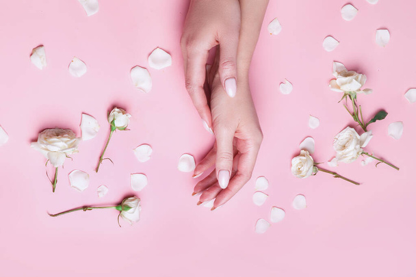 Woman's hand with natural manicure and flowers of white roses on pink background - Fotoğraf, Görsel