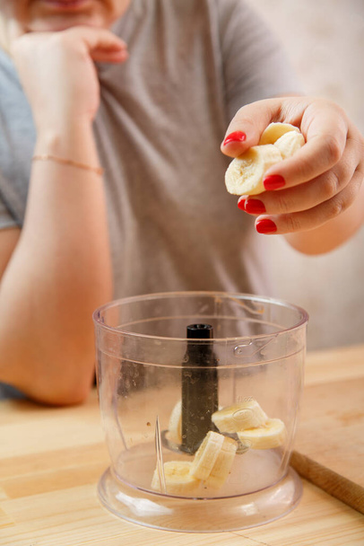 A female hand puts banana slices in a blender bowl. - 写真・画像