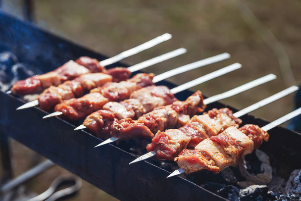 Shish kebab in the nature of an outsider. Raw skewers meat on skewers on the barbecue grill. Cooking shashlik on a live fire - Photo, Image