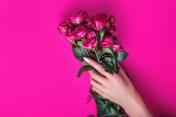 Female hand holding bouquet of pink roses flowers on pink background. Holiday background, top view. Flat lay - Foto, afbeelding