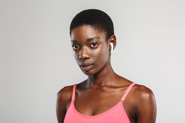Image of african american sportswoman using wireless earbuds and looking at camera isolated over white background - Fotó, kép