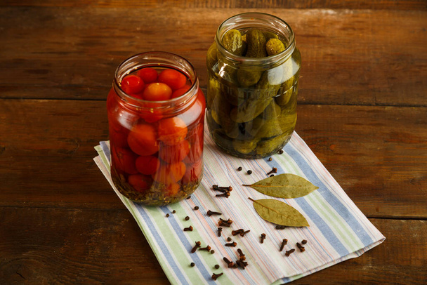 Jars of pickled cucumbers and cherry tomatoes homemade pickling on a linen towel on a wooden table. - Foto, Imagem
