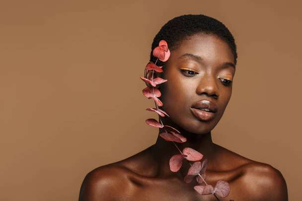 Beauty portrait of pretty young half-naked african woman holding exotic flower isolated over brown background - Φωτογραφία, εικόνα