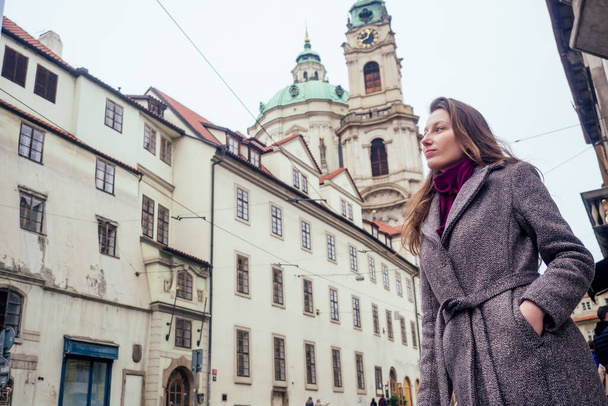 Outdoor portrait of young beautiful fashionable woman wearing trendy jacket with small shoulder bag, walking in street of european Chezh Praha city - Foto, imagen