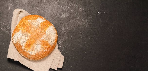 One bun of freshly baked bread on a black background. The concept of minimalism food. Flat layout - Photo, Image