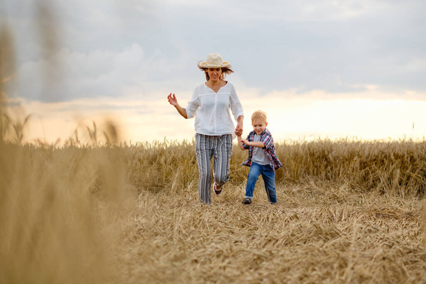 Madre e figlio felici stanno correndo attraverso un campo di grano in estate
 - Foto, immagini
