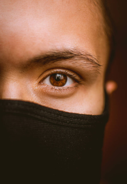половина лица человека в черной маске с карими глазами во время пандемии коронавируса
 - Фото, изображение