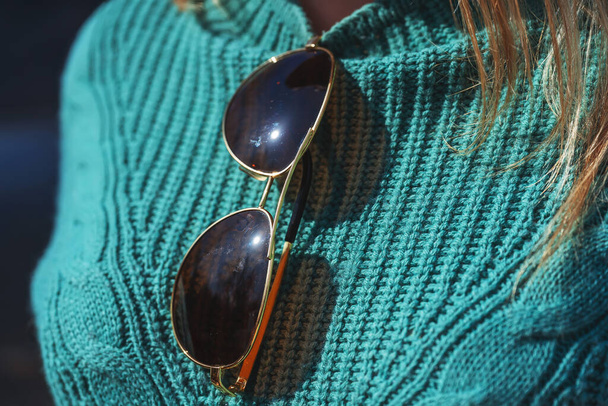 Napszemüveg egy nő pulóverén közelről. Régi, koszos napszemüveg. Napszemüveg barna üveggel és arany kerettel - Fotó, kép