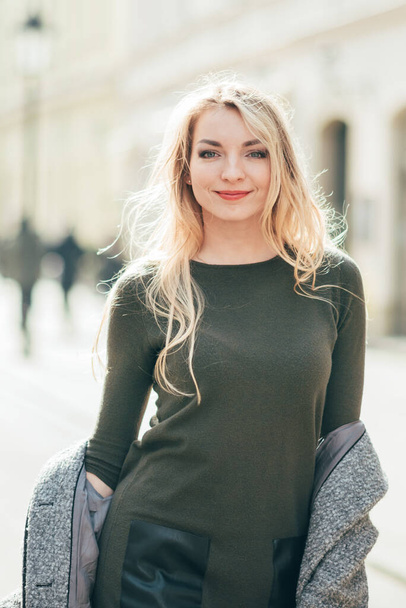 Close up portrait of young blond beautiful woman walking on city street, europe vacation, holding little bouquet, smiling, walk in krakow, grey coat, beautiful young woman walking on the street - Fotó, kép
