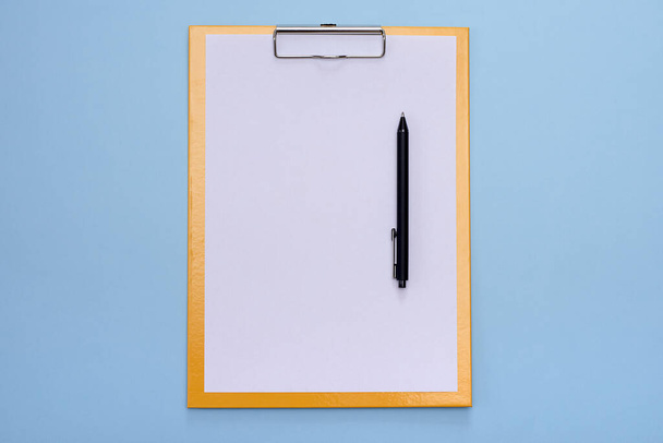 Un portapapeles amarillo y una pluma negra con papel blanco en blanco sobre un fondo azul. Copiar espacio
. - Foto, Imagen