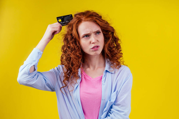 Confused redhaired ginger curly woman colding plastic creditcard and looking upsad .rejection concept - Foto, afbeelding