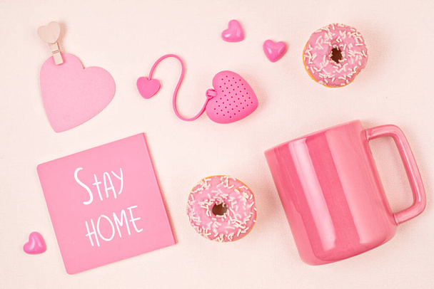 Flache Liege mit rosa Accessoires, Teetasse und Donuts auf hellrosa Hintergrund. Ansicht von oben. Morgens Rituale, zu Hause bleiben - Foto, Bild