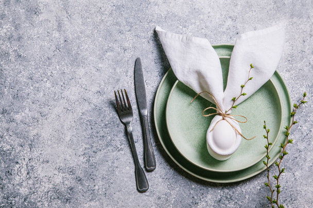 Happy easter concept. Easter bunny. Easter egg in a plate and branches with buds on a gray background. Flat lay, top view, copy space. - 写真・画像