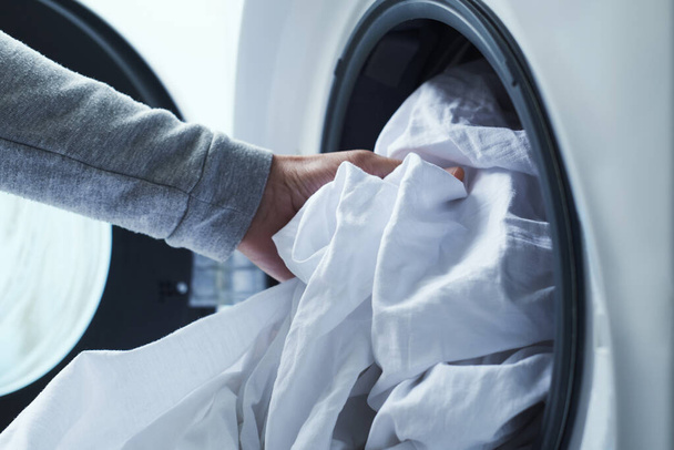 close-up van een jonge blanke man zetten wit beddengoed in de wasmachine - Foto, afbeelding