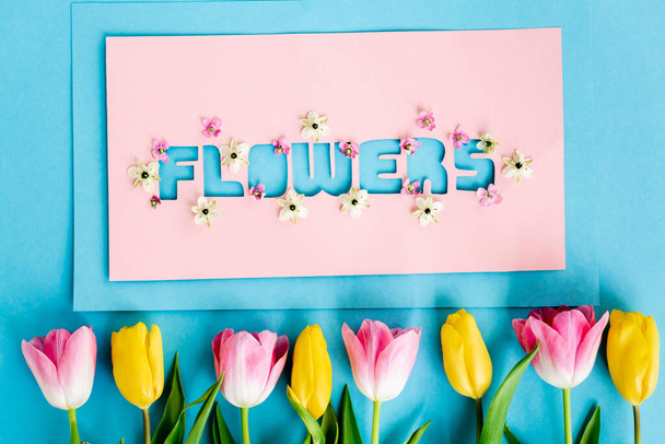 top view of yellow and pink tulips near greeting card with flowers lettering on blue, mothers day concept  - Foto, immagini