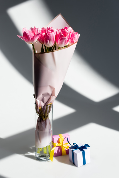 sunlight on pink tulips in vase near gift boxes on white, mothers day concept - Foto, immagini