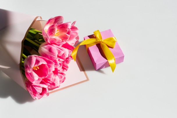 sunlight on pink tulips near gift box on white, mothers day concept - Фото, изображение