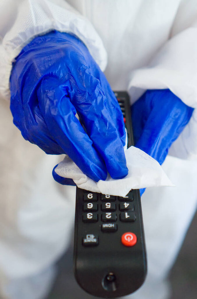 Hand in protective glove with napkin cleaning remote control. Covid-19 disinfection concept. - Photo, image