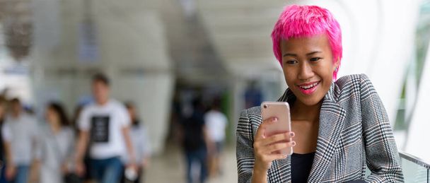 Portrait of young rebellious Asian businesswoman with pink hair at footbridge in the city outdoors - Фото, зображення