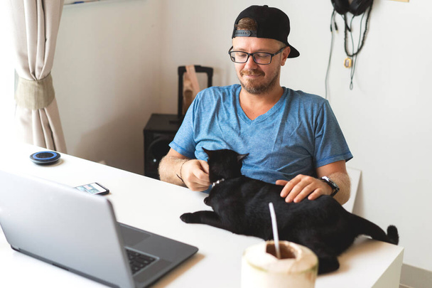 freelancer guy with laptop and cat  working at home in quarantine to coronavirus infection  - Фото, изображение