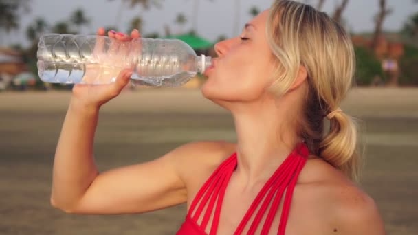Joven mujer atractiva en un traje de baño bebe agua de una botella
 - Metraje, vídeo