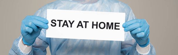 Vista ritagliata del medico in possesso di carta con soggiorno a casa lettering isolato su grigio, colpo panoramico
 - Foto, immagini