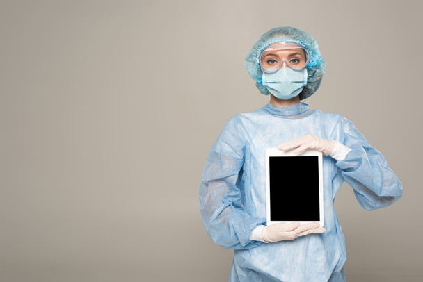 Médico en googles de seguridad y máscara médica sosteniendo tableta digital con pantalla en blanco aislado en gris
 - Foto, imagen