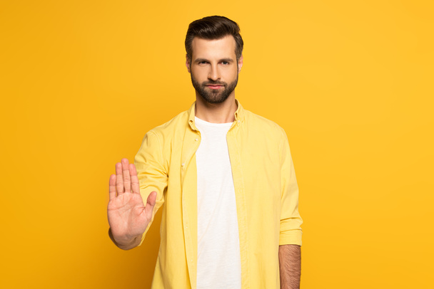 Handsome man showing stop sign on yellow background - Photo, Image