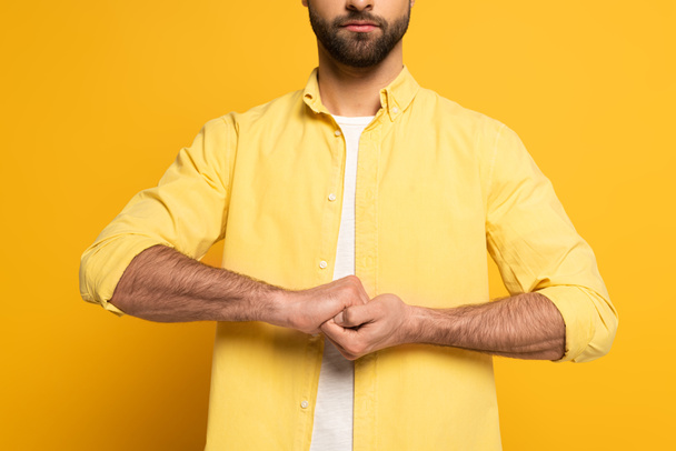Cropped view of man showing cohesion sign in deaf and dumb language on yellow background - Foto, afbeelding