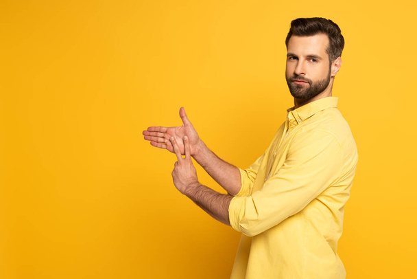 Side view of young man showing sign in deaf and dumb language on yellow background - Foto, immagini