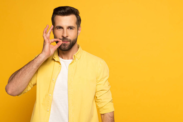 Handsome man using sign language and looking at camera on yellow background - Φωτογραφία, εικόνα