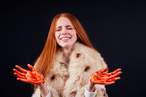 sad redhaired ginger fashion victim woman with blood on her hands wearing natural fur coat and crying,studio black background.stop animal killing please - Fotó, kép