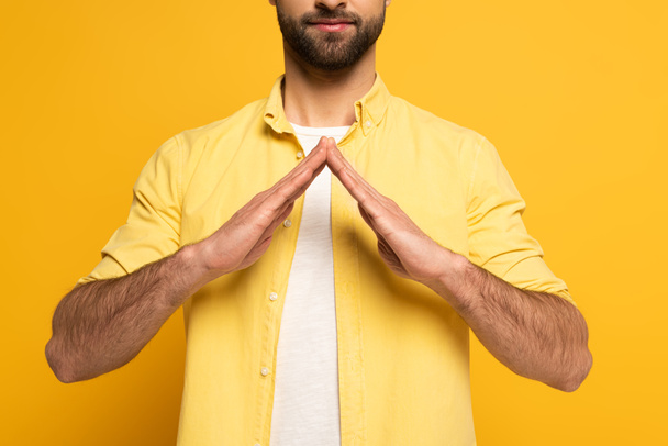 Cropped view of man showing house sign in deaf and dumb language on yellow background - Foto, imagen