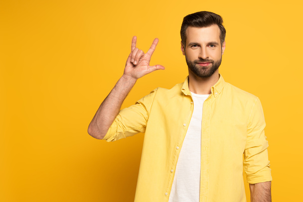 Hombre guapo mostrando palabra amor en lenguaje de señas sobre fondo amarillo
 - Foto, imagen