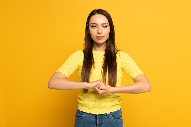 Young woman showing marriage sign in deaf and dumb language on yellow background - Fotoğraf, Görsel