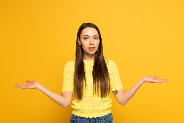 Atraktivní dívka ukazuje pokrčení rameny gesto na žlutém pozadí - Fotografie, Obrázek