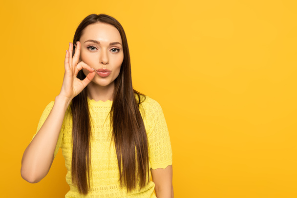 Woman with hand near mouth showing sign from deaf and dumb language on yellow background - Fotoğraf, Görsel