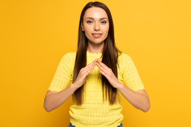 Smiling girl showing home gesture in deaf and dumb language on yellow background - Фото, изображение