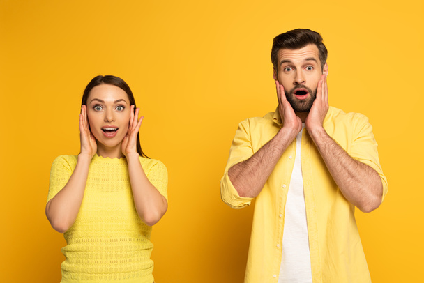 Surprised young couple looking at camera on yellow background - 写真・画像