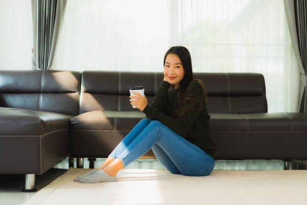 Portrait beautiful young asian woman use smart mobile phone with coffee cup with sofa in living room interior - Foto, afbeelding